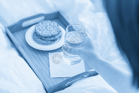 女性手在托盘上举着水杯 床上装着饼干玻璃营养蓝色桌子饮食食物白色节食早餐图片