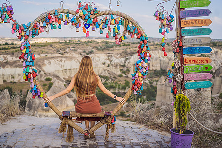 年轻女子在土耳其卡帕多细亚的格雷梅附近探索带岩层和仙女洞穴的山谷 许愿树 有铭文的小多色水罐 挂在树枝上的愿望 在沙废墟和蓝天的图片