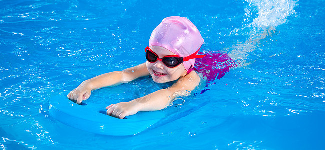 微笑的小女孩在游泳课上学习用在游泳池里游泳的全景图片