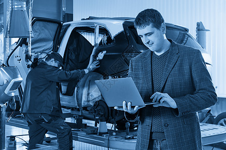 经理拿着笔记本电脑站在汽车修理店的汽车附近 背景是机械师修理汽车车辆控制引擎机械男性男人运输检查调子发动机图片