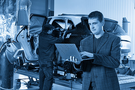 经理拿着笔记本电脑站在汽车修理店的汽车附近 背景是机械师修理汽车车站运输职业服务机械工作车库男人男性调子图片