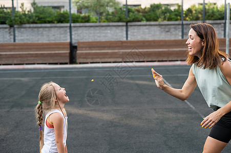 妈妈和女儿在户外运动场上玩得开心 一个高加索女人扔糖果 一个女孩用嘴捡到糖地面母亲行动孩子微笑女孩育儿成人女性乐趣图片