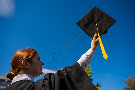 一个女人把她的毕业帽扔在蓝天上快乐天空幸福文凭女性蓝色仪式空气帽子学生图片