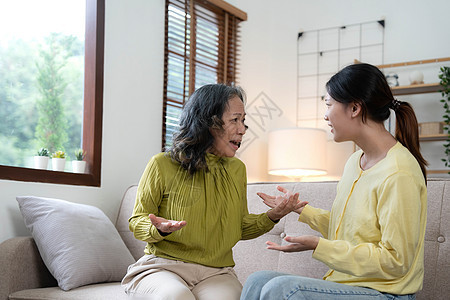 家人坐在沙发上发生争执 成年女儿证明自己的权利积极与年迈的母亲争论 60 多岁的母亲因误解而绝望 代沟 家庭观念冲突愤怒敌意罪行背景图片