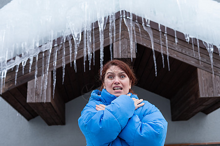 一个惊恐的女人站在一个有大冰棒的屋顶下 冬天很危险温度冒险女性冰柱门廊水晶季节天气眼镜农村图片