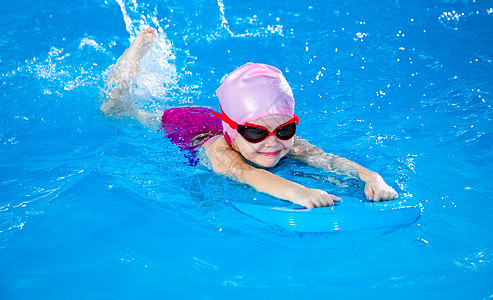 学龄前可爱的小女孩 学会在室内游泳池里游泳班级漂浮运动浮板水池泡沫风镜女孩木板训练背景图片