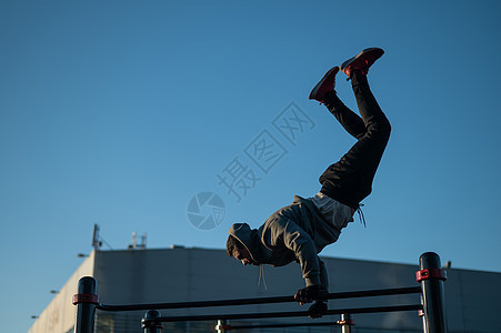 年轻的caucasian男子在室外做平行的酒吧运动男人耐力竞赛腹部活力蓝色运动员体操帽衫肌肉图片