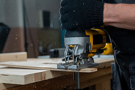 一名男子在车间用电锯砍木板的缝合装置上乐器建设者拼图工作台桌子裁剪木材锯末工具工艺图片