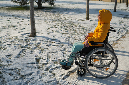 白种残疾妇女在冬季坐在公园的椅子上 女孩在轮椅上散步时骑着椅子图片
