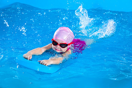 学龄前可爱的小女孩 学会在室内游泳池里游泳女孩漂浮练习水池蓝色游泳衣木板班级泡沫游泳者图片