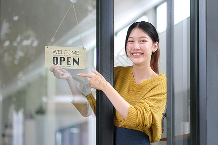 年轻亚洲经理女孩改变一个标志 从特写到开放 在门咖啡厅上 她看着门外等待被锁后客户 拥有小生意 食品和饮料 企业重新开业的概念女图片