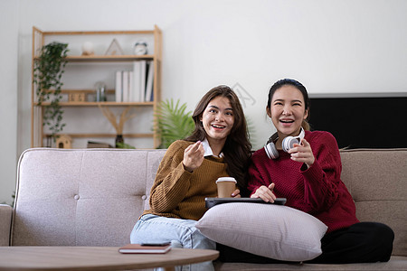 两个年轻的女人在家里的客厅里坐在沙发上看电视 高兴地握着拳头庆祝最喜欢的运动队的胜利 周末休闲 电视节目和娱乐概念微笑手表房间喜图片