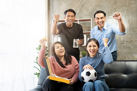 朋友们在电视上观看体育 欢呼和庆祝 不同亚洲朋友的支持者们愉快地坐在沙发上团队情感娱乐女士长椅快乐闲暇男性扇子团体图片