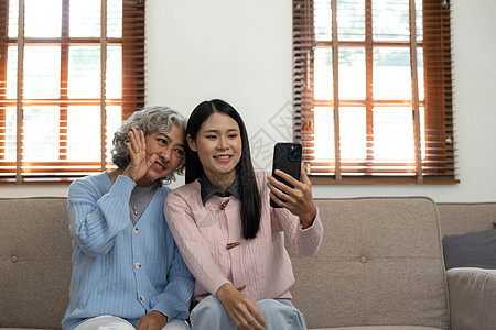 微笑的年长母亲和成年女儿一起使用电话 坐在家里舒适的沙发上 快乐的年轻女人和成熟的妈妈看着智能手机屏幕 看视频 玩得开心 两代人图片