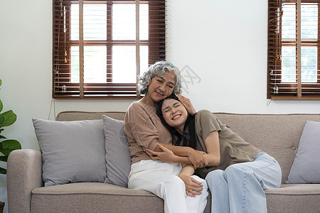 亚洲可爱家庭的画像 小女儿抱着年长的母亲 迷人的女人和年长的成熟妈妈坐在沙发上 在客厅里一起享受家里的活动 微笑 看着镜头老年喜图片