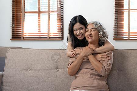 慈爱的成年女儿拥抱年长的母亲 站在家里的沙发后面 家人一起享受温柔的时刻 年轻女人和成熟的妈妈或祖母互相看着 两代人孙女女性快乐图片