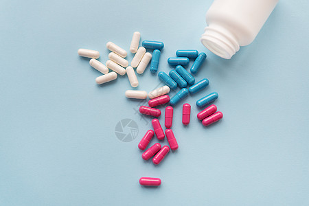 各种彩色药丸 — 蓝色 粉色 白色从一个打开的塑料瓶中飞出 在浅蓝色背景中被隔离图片