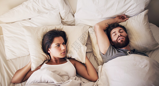 今天你要去一个睡眠诊所 一位年轻女人用枕头遮住她的耳朵 而她的丈夫在床上打呼噜图片