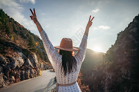 穿着棕帽子和白色毛衣的女旅行者 看着惊人的山峰和森林 漫游概念 大气史诗时刻树木晴天冒险假期游客荒野自由旅行远足者女性图片