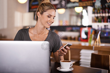 无线技术和一杯热饮 一个美丽的年轻女子在咖啡店里使用她的手机图片