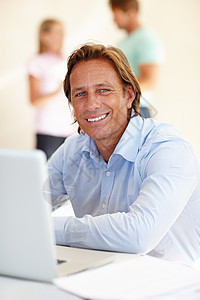 他知道他的辛勤工作是值得的 在灯火通明的办公室里 一个微笑的男人在办公桌前使用笔记本电脑图片