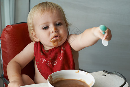 成长中的男孩需要食物 一个年轻的小男孩在高椅子上吃着心的肉消耗品孩子儿童男婴勺子金发女郎男性男孩们青年童年图片