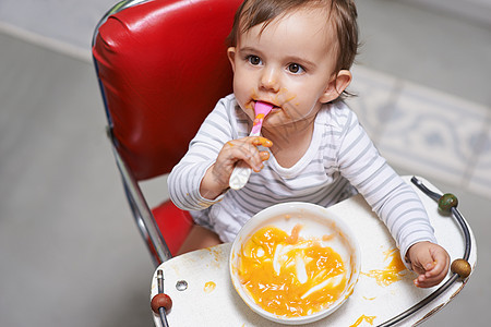 新品味的探索 一个可爱的小婴儿坐在高架上吃着坚固的食物图片