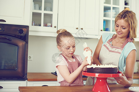 小心地在新鲜蛋糕上涂上糖霜 可爱的小女孩和她妈妈在厨房里给蛋糕抹糖霜图片