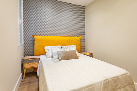 以床为中心的卧室内部铺满了奶油色提花床罩 枕头整齐地堆放在灰色墙壁的黄色床头板上 两侧的床头柜采用复古风格图片