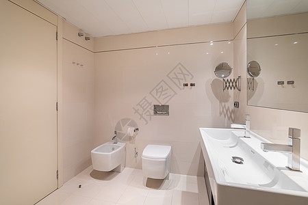 大浴室装有米砖 整面镜子和长方形水龙头 有两个水龙头 厕所和浴缸图片