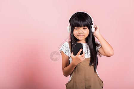10年的亚洲小孩享受手机听音乐 并佩戴无线耳机粉色青春期女性音乐孩子们紫色工作室细胞耳机童年图片