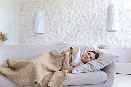 一个疲劳的女人躺在沙发上 被毯子覆盖着的睡在床上 病了 感觉不好 沮丧图片