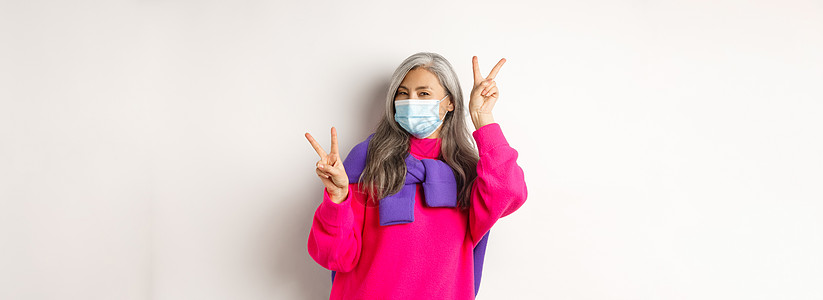 Covid 流行病和社会疏远概念 站在白色背景上 戴着医用面具 展示和平标志的开朗时尚的亚洲高级女性化妆品购物广告疾病奶奶成人母图片