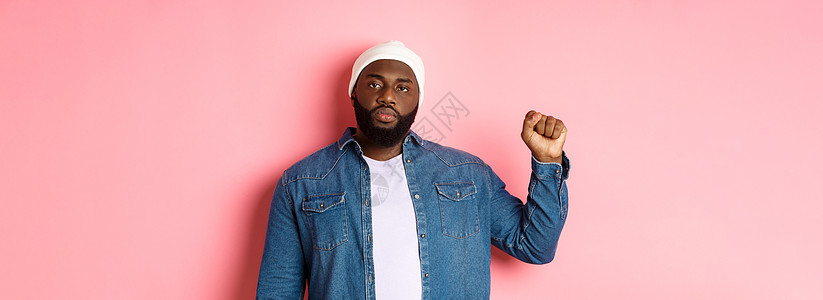 严肃而自信的非裔美国男性活动家 举起拳头 支持黑人生命问题 BLM 运动 争取人权反对种族主义 粉红色背景胡须生活横幅帽子潮人男图片