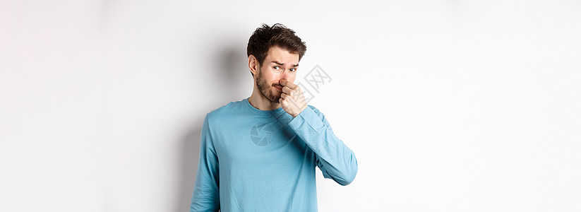 穿着运动衫的恶心青年男子 闭上鼻子 看着臭气熏天的东西 站在白背景上站着胡子情绪生活男人胡须商业广告发型促销工作室图片