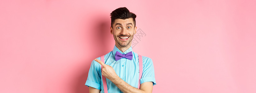 英俊的caucasians男子与棕榈和胡子 指向右侧 展示广告 站在粉红背景上 在优雅的弓领快乐工作室情绪发型男人商业成人吊带裤图片