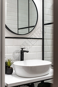 洗手间有白砖墙 黑色水龙头 白色桌边的奥瓦尔浴缸 黑框墙上的圆镜图片
