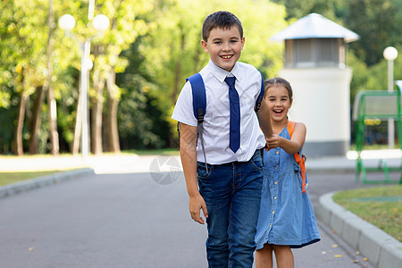 女孩和男孩穿着白衬衫 在夏天阳光明媚的一天早上背着背包图片