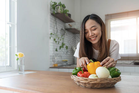 穿着围裙站在厨房里的年轻快乐女人的画像 准备用新鲜蔬菜和水果烹制健康食品女孩烹饪营养成人微笑家庭乐趣饮食房子午餐图片