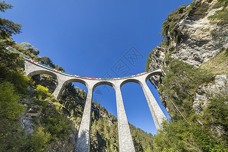瑞士列车经过瑞士格劳本登阿尔卑斯山桥轨道溪流交通悬崖低角度旅行曲线乡村建筑学假期图片