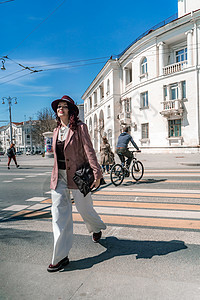 女人城市道路交叉口 戴着帽子的时尚女人在城市的人行横道过马路 身着白色长裤和外套 手里拎着一个包运输人士街道闲暇商务运动季节天气图片