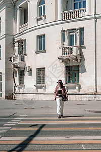 女人城市道路交叉口 戴着帽子的时尚女人在城市的人行横道过马路 身着白色长裤和外套 手里拎着一个包头巾街道斑马女性魅力季节商务天气图片