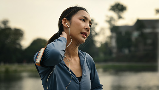 美丽的女运动员在户外跑步后休息 站在湖边 背景是阳光明媚的风景图片