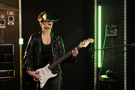 带虚拟现实耳机的吉他手一边用电吉他演奏重金属歌曲一边享受摇滚音乐会模拟图片