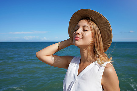 带着帽子微笑的女孩 呼吸着新鲜空气 背景是蓝海蓝色冥想晴天护理沉思天空皮肤瑜伽日光浴女性图片