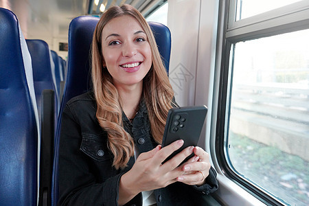 年轻女商务人士使用公共交通工具 坐在火车上与电话同坐 看着摄像机女性商业互联网运输通勤者拉丁座位阅读城市交通图片