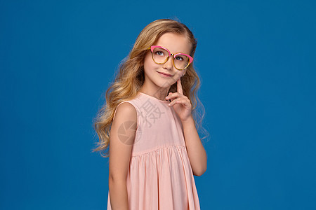 穿着粉红色裙子和眼镜的时装小女孩 站在蓝色背景上 笑声配件孩子女孩皮肤女性金发童年耳朵教育头发图片