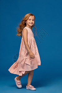 穿粉红色裙子的时装小女孩 穿着蓝色背景的衣服眼睛卷曲头发肩膀女儿玫瑰耳朵女士皮肤微笑图片