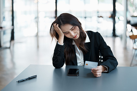 年轻亚裔女性持有智能手机信用卡 在信用卡债务上表现忧心忡忡的表情 这让她们一目了然水平电脑金融女士店铺互联网零售技术卡片网上购物图片