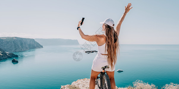 一位骑山地自行车的女自行车手 眺望山海风光 站在海边的骑自行车的女人的后视图 张开双臂 自由和健康的生活方式理念图片